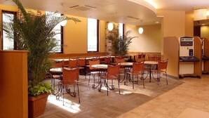 Um hall de hotel com várias mesas e cadeiras, plantas grandes em vasos e uma área de recepção.