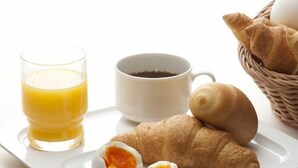Uma bandeja de café da manhã com um croissant, um copo de suco de laranja e uma xícara de café.