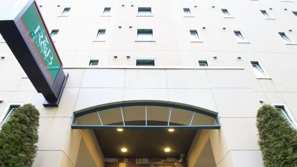 Entrada de hotel com design moderno, fachada de tijolos, placa indicativa verde e área de acesso com azulejos.