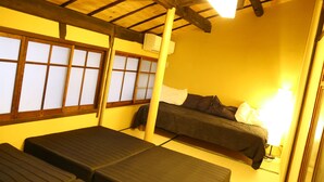 A room with tatami flooring, a low bed, a sofa, a window with shoji screens, and a ceiling fan.