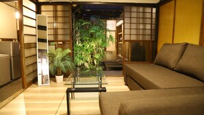 A living room with a sofa, a glass coffee table, a potted plant, and a sliding door leading to another room.