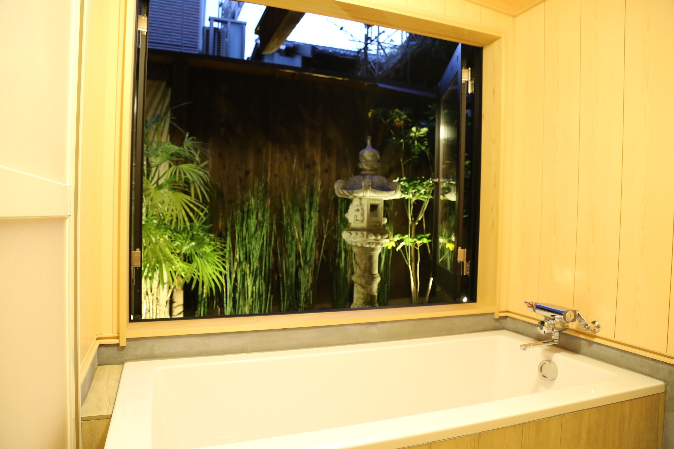 A bathroom with a large window, a bathtub, and a wooden wall.