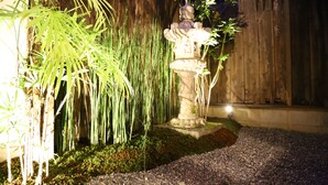 A garden with a stone fountain, bamboo plants, and a wooden fence.