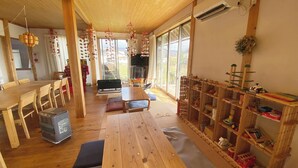 A spacious room with a wooden dining table, chairs, a sofa, and a bookshelf filled with toys. - Tabinoyado Tenohirani Taiyonoie (Tome)