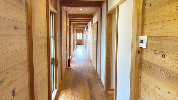 A wooden hallway with a fire extinguisher, a thermostat, and a door at the end. - Tabinoyado Tenohirani Taiyonoie (Tome)