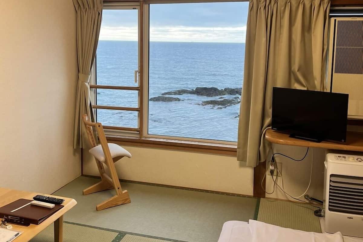 Een kamer met een bed, een bureau, een stoel, een televisie en een raam met uitzicht op de oceaan.