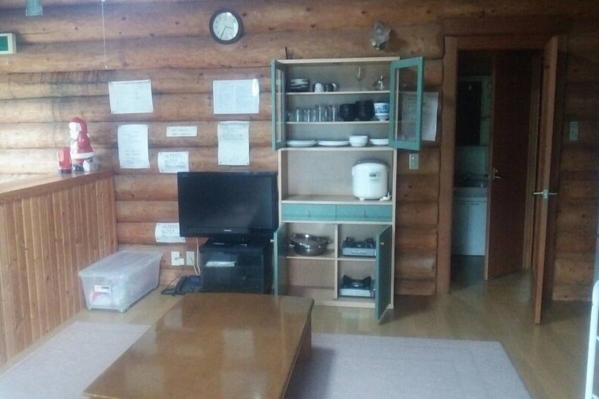 Interior d'una cabana de fusta amb terra de fusta, una televisió, una estant plena de plats i un rellotge a la paret.