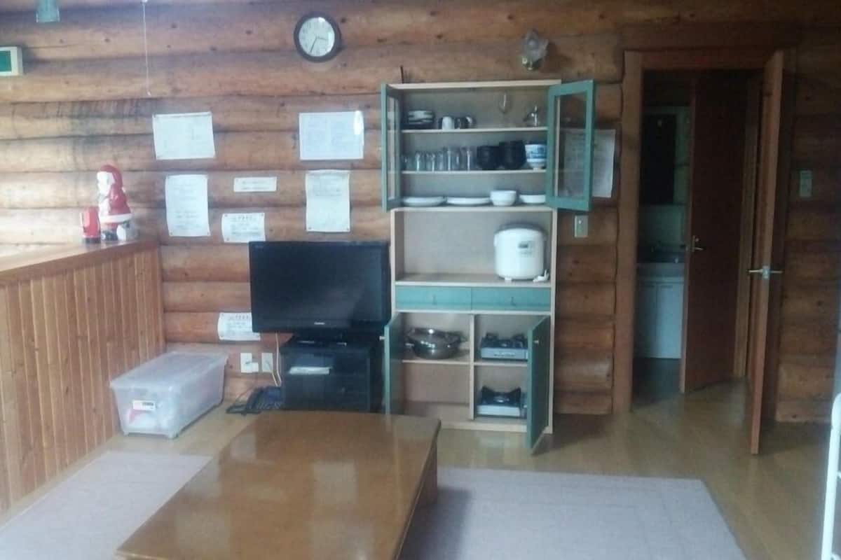 L’intérieur d’une cabane en rondins, avec un plancher en bois, un téléviseur, une étagère remplie de vaisselle et une horloge au mur.