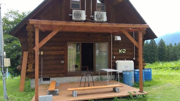 A wooden cabin with a porch, two air conditioning units, a bench, a table, and a door marked 'K2'. - Tm Resrot Kijimadaira (Kijimadaira)