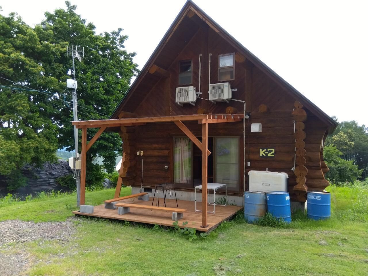 Een houten chalet met een veranda, airconditioners en het nummer 'K2' op de deur.