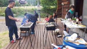 A wooden deck with barbecue grills, a table with food and drinks, and a rustic cabin in the background. - Tm Resrot Kijimadaira (Kijimadaira)