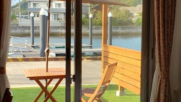 Habitación de hotel con un ventanal grande, una cama y vistas a una zona verde con mesa y sillas afuera.