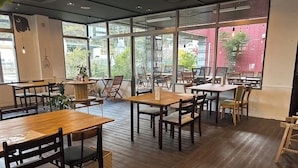 Un comedor interior con mesas y sillas de madera, ventanas amplias y vistas al exterior.