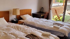 Una habitación de hotel con dos camas, una mesita de noche con lámpara, un escritorio pequeño y una silla.