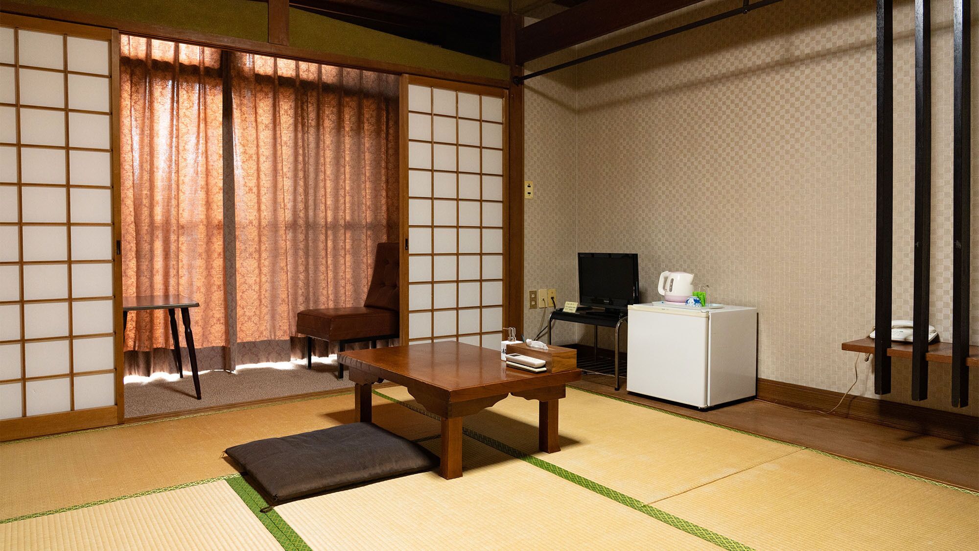 Une pièce de style japonais traditionnel, avec un sol recouvert de tatamis, une table basse, une chaise, un téléviseur et un réfrigérateur.