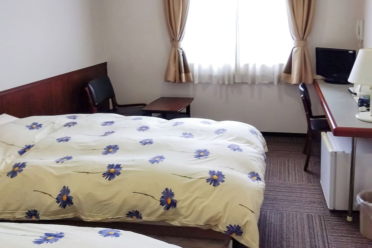 A hotel room with a bed, a desk, a chair, and a window with curtains.