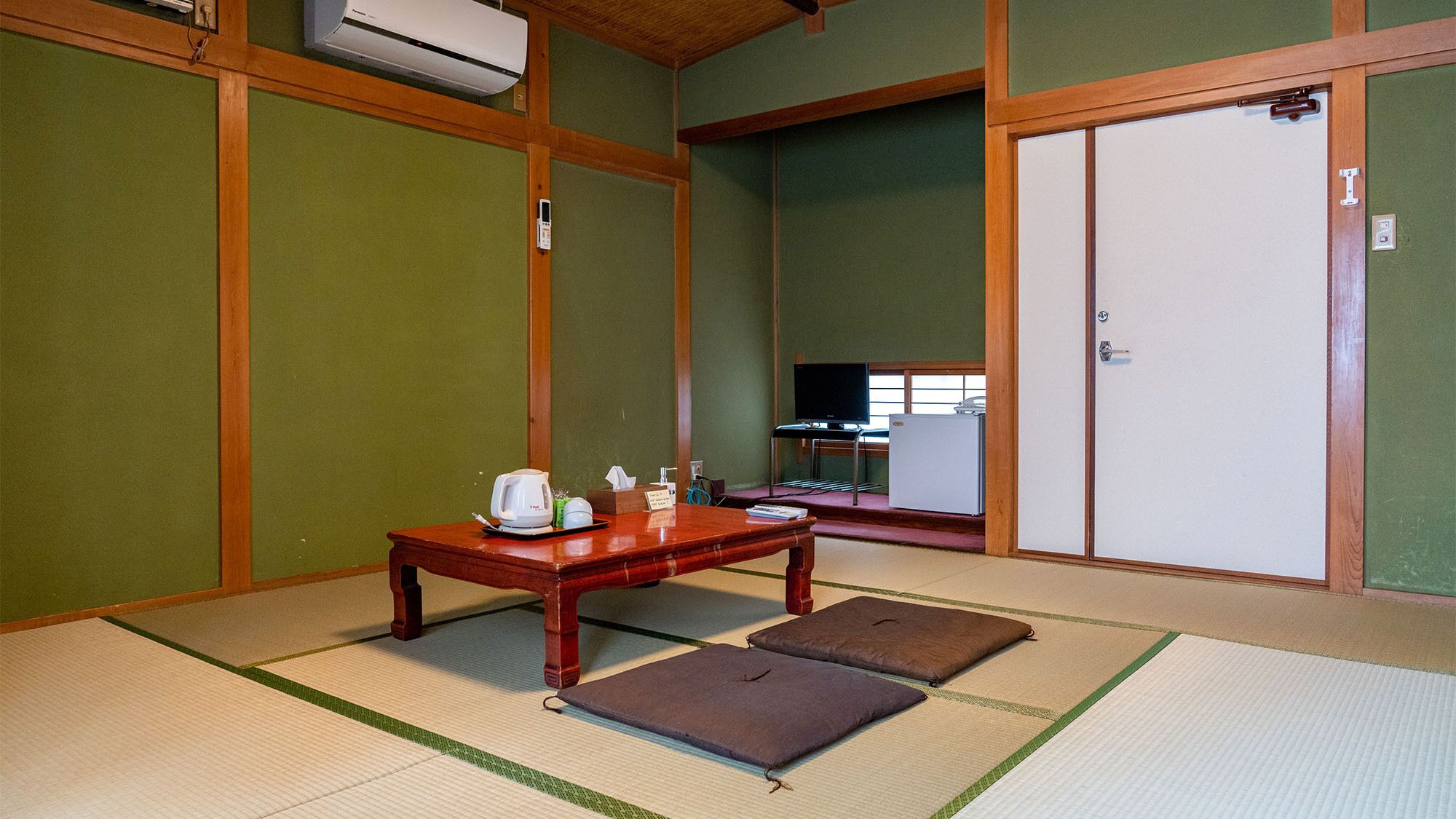 Une pièce de style japonais traditionnel, avec un sol recouvert de tatamis, une table en bois, une bouilloire, un téléviseur et un réfrigérateur.