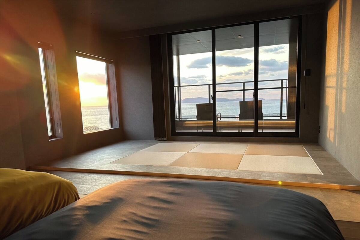 Ein Zimmer mit einer großen Schiebetür zu einem Balkon mit Blick auf das Meer und die Berge.