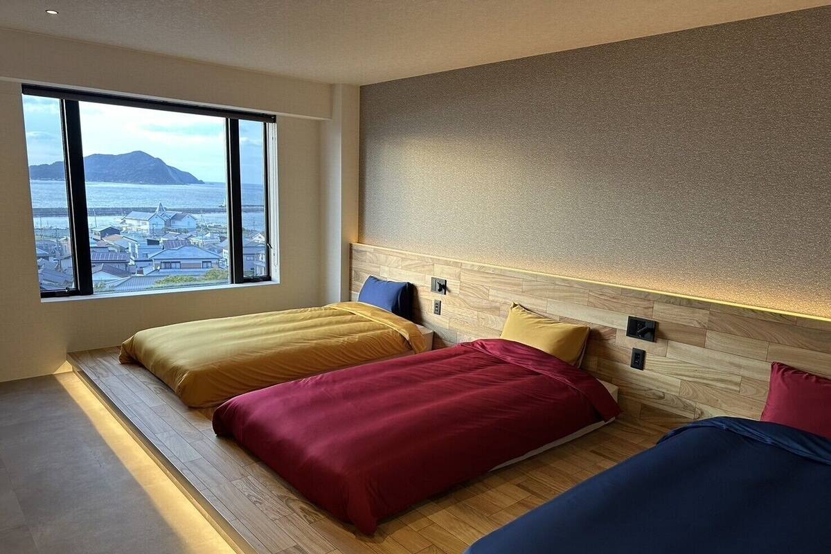 Ein Hotelzimmer mit zwei Betten, einem großen Fenster mit Blick auf eine Stadt und Berge, sowie einem Holzboden.