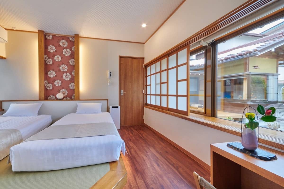 Quarto com duas camas, piso de madeira, janela com vista e escrivaninha com um vaso.