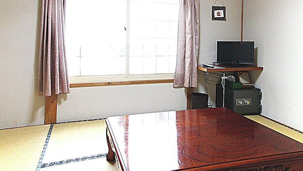 A room with a tatami mat, a wooden bed, a TV on a stand, a small safe, and a window with curtains. - Nozawa Onsen Yamaya Sanso (Nozawaonsen)