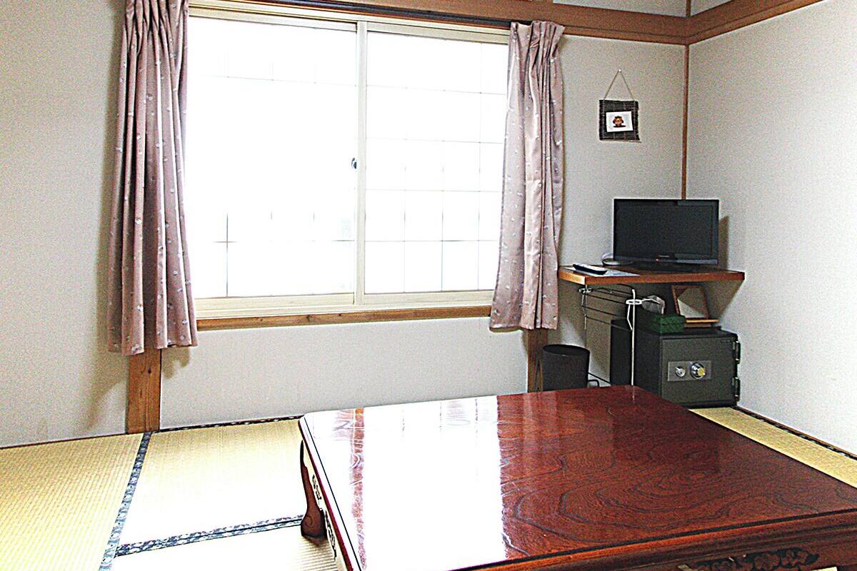 A room with a tatami mat, a wooden bed, a TV on a stand, a small safe, and a window with curtains.