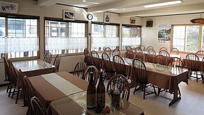 A conference room with multiple tables and chairs, large windows, and ceiling lights. - Nozawa Onsen Yamaya Sanso (Nozawaonsen)