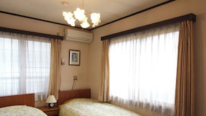 A hotel room with two beds, a nightstand, a lamp, an air conditioning unit, and a ceiling light fixture. - Nozawa Onsen Yamaya Sanso (Nozawaonsen)