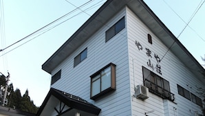 A multi-story building with a flat roof, a visible entrance with a small porch, and a sign with Japanese characters. - Nozawa Onsen Yamaya Sanso (Nozawaonsen)