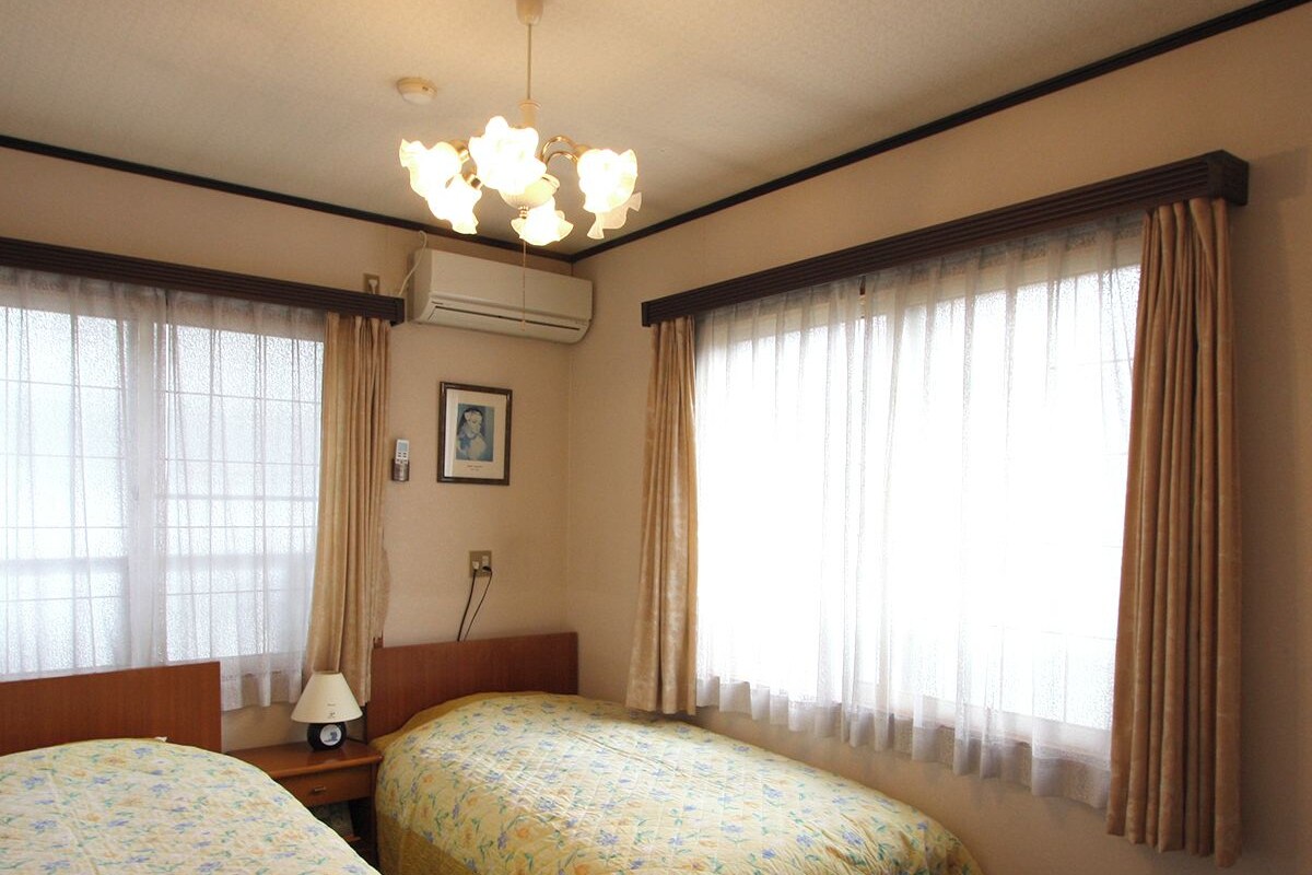 A hotel room with two beds, a nightstand, a lamp, an air conditioning unit, and a ceiling light fixture.