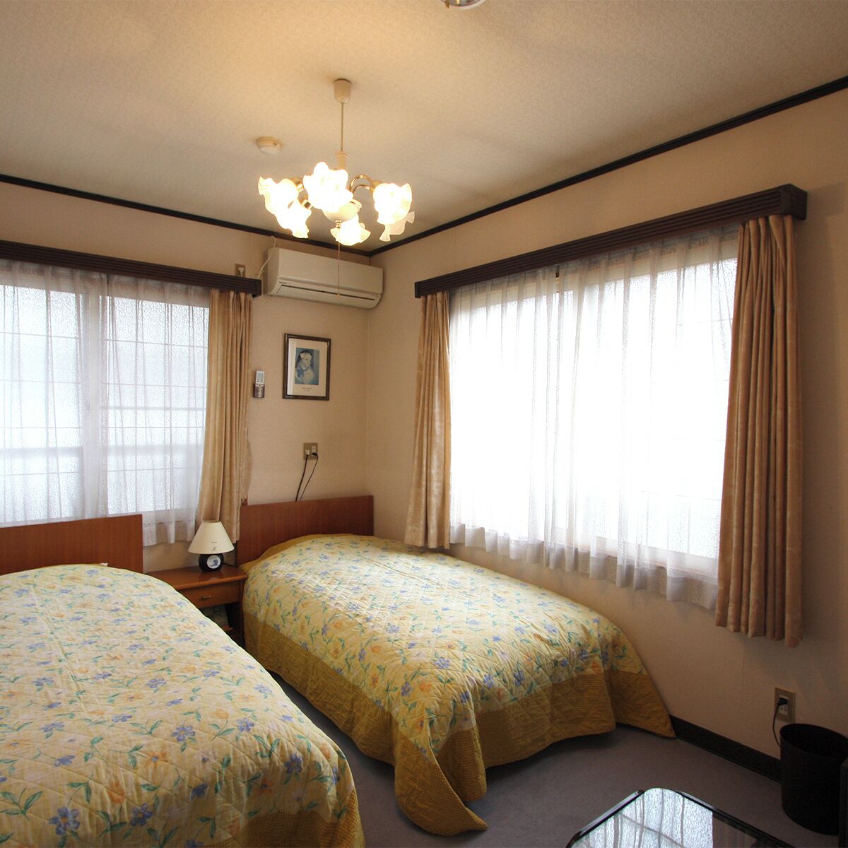 A hotel room with two beds, a nightstand, a lamp, an air conditioning unit, and a ceiling light fixture.