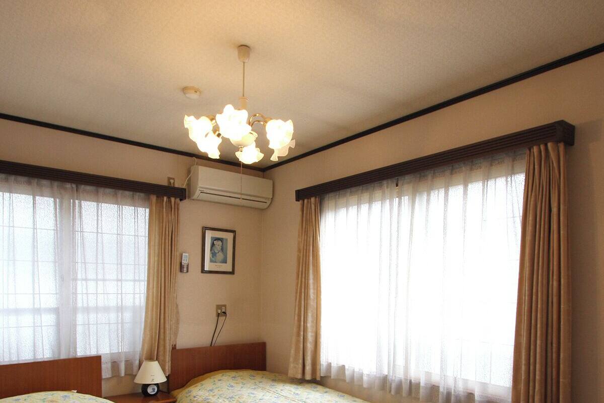 A hotel room with two beds, a nightstand, a lamp, an air conditioning unit, and a ceiling light fixture.