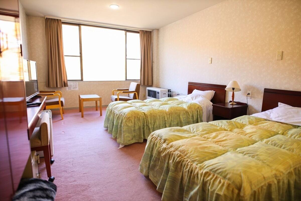 Une chambre d’hôtel avec deux lits, un bureau, une chaise, une télévision et une fenêtre avec des rideaux.