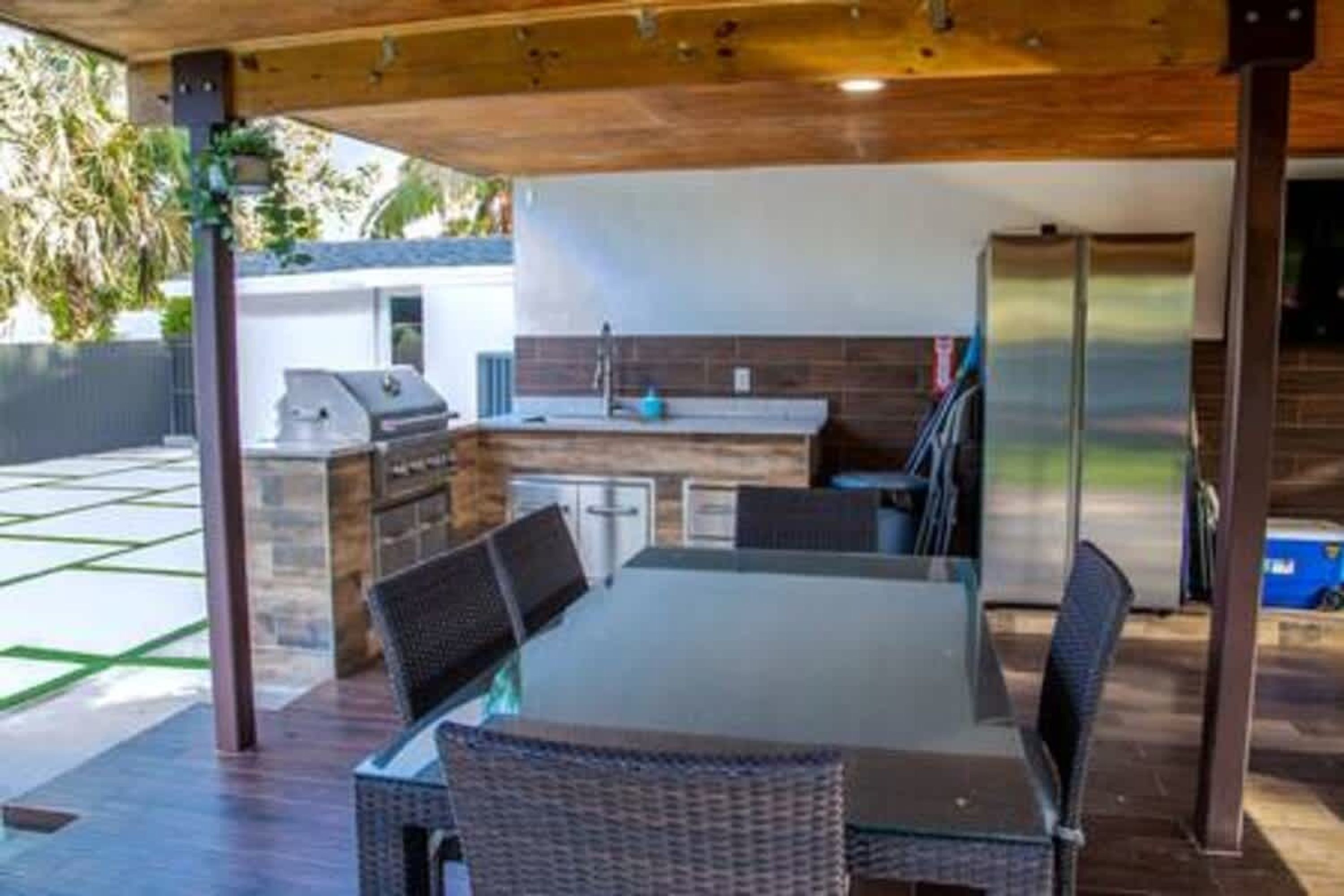 An outdoor kitchen with a dining table and chairs, a grill, and a refrigerator.
