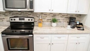 A kitchen with a microwave, stove, cabinets, and a tiled backsplash. - Ocean Breeze Bungalow 4BR 2BA W Pool (Hollywood)