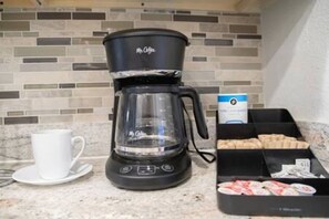 Uma cafeteira, uma chávena e uma caixa de pastelaria numa bancada de cozinha.
