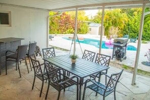 Een overdekt terras met een zwembad, tuinmeubels en een barbecuehoek.
