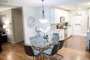 Een moderne keuken met witte kasten, een glazen eettafel en een hanglamp.