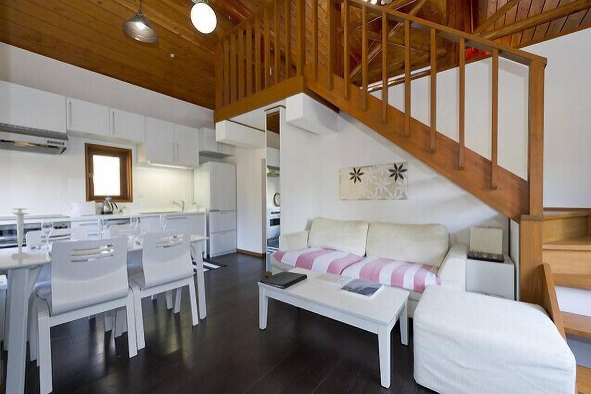 A modern interior with a dining area, a sofa, a staircase, and a kitchen.