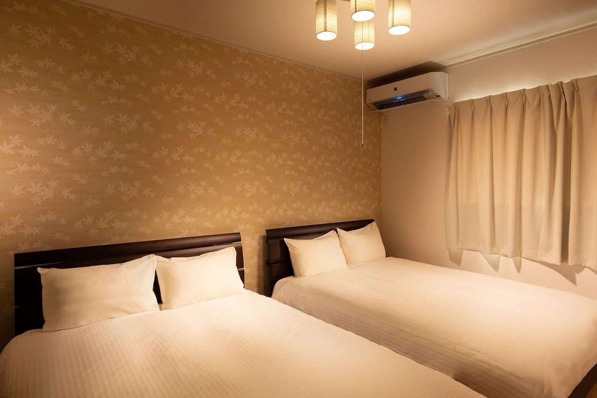 Ein Hotelzimmer mit zwei Betten, einem Deckenventilator, einer Klimaanlage und einem Fenster mit Vorhängen.