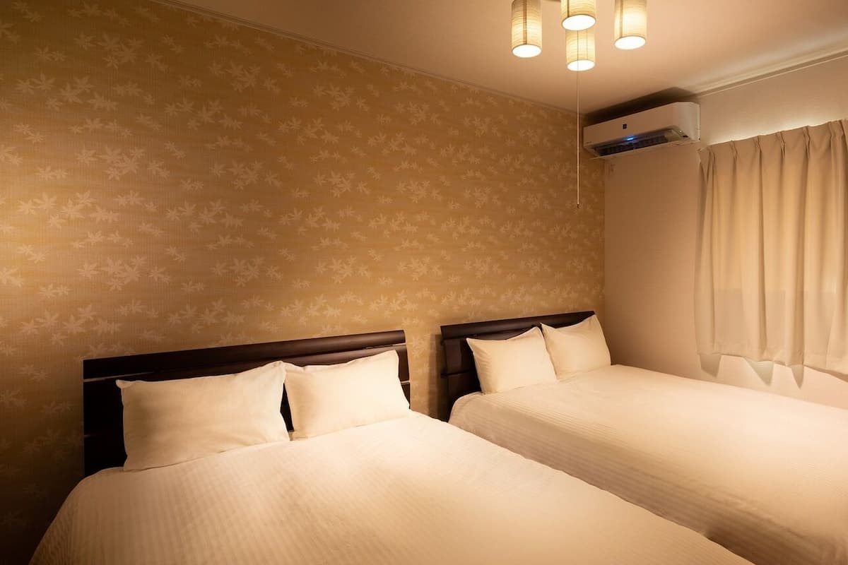 Ein Hotelzimmer mit zwei Betten, einem Deckenventilator, einer Klimaanlage und einem Vorhangfenster.