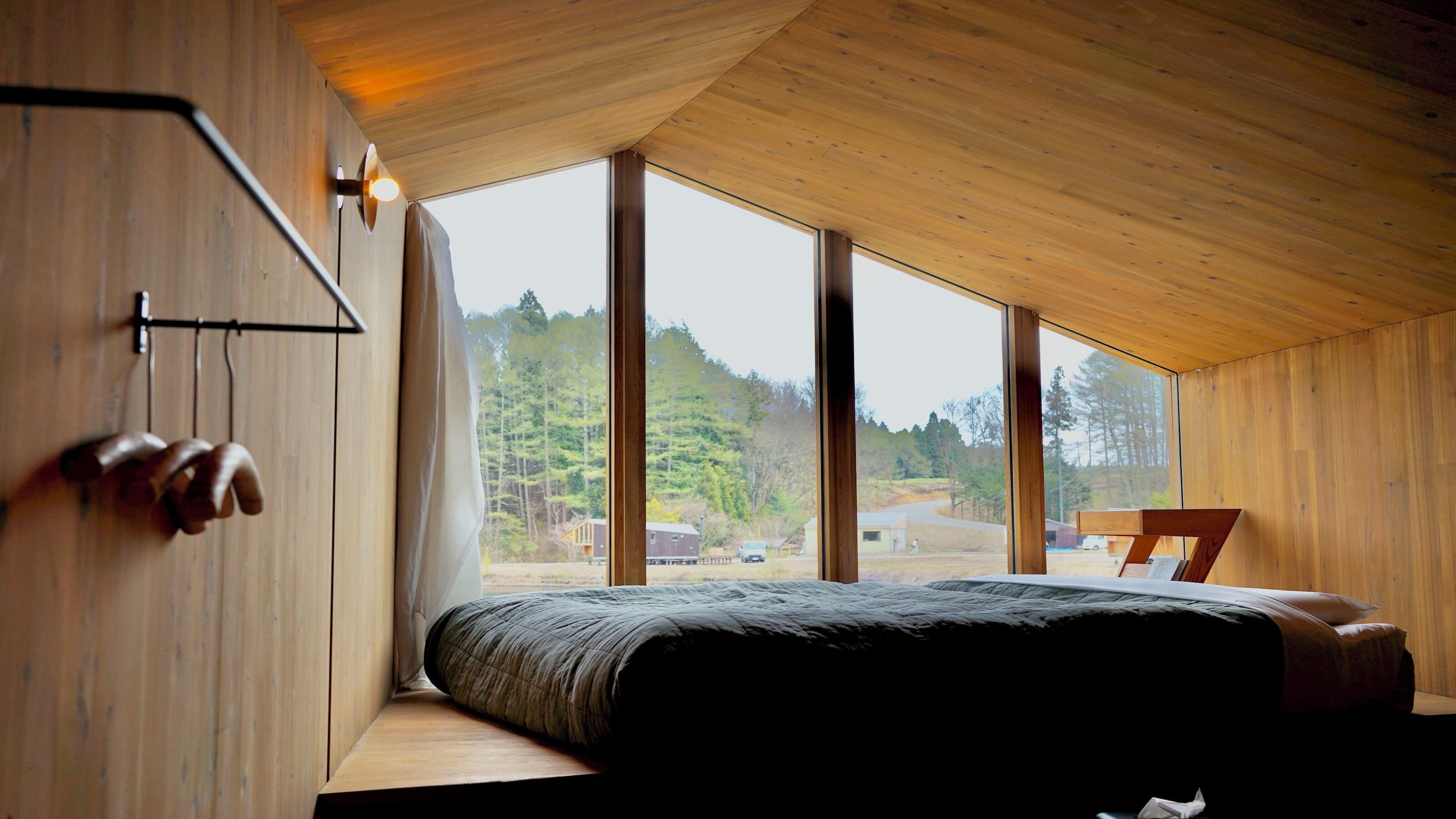 Een slaapkamer met een groot raam, houten wanden en een bed met een donkerdeken.