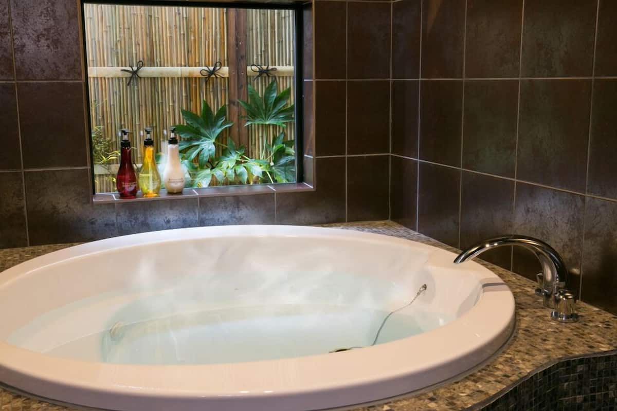 A bathroom with a large bathtub, a window with plants, and a sink.