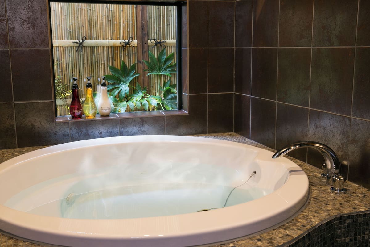 A large bathtub with a window above it, a sink, and a faucet.