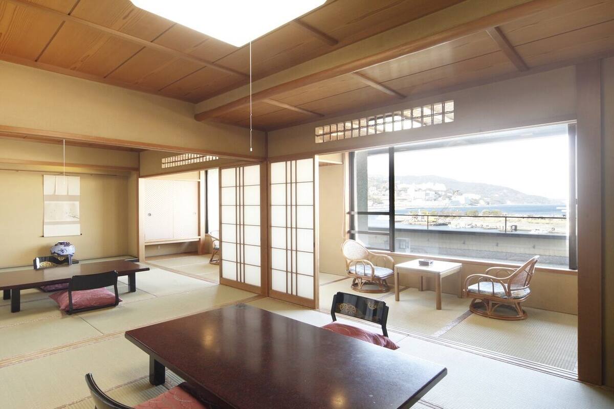 Une pièce de style japonais traditionnel, avec un sol recouvert de tatamis, une petite table en bois et des portes coulissantes donnant sur un balcon avec vue.