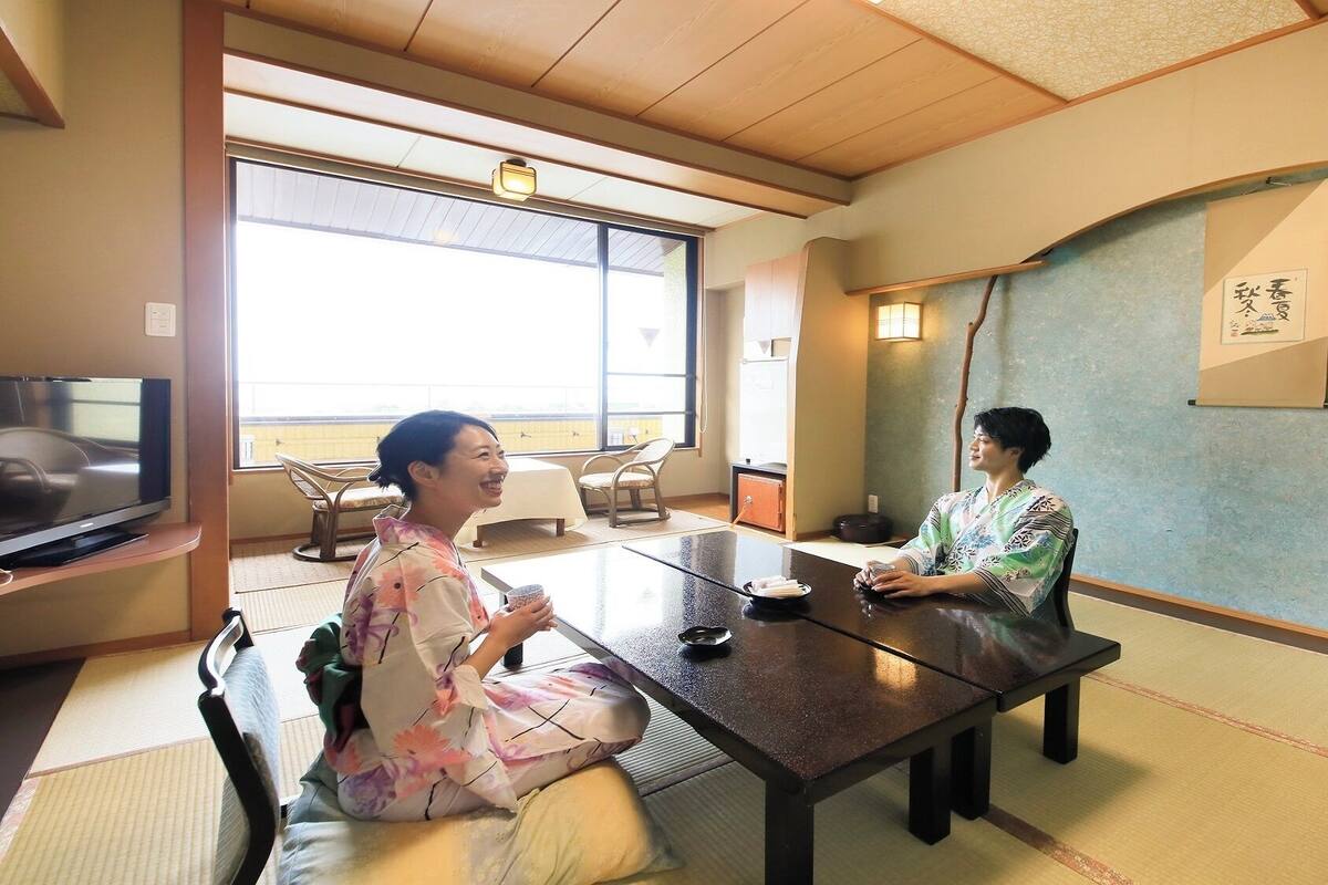 Une pièce de style japonais traditionnel, avec un sol recouvert de tatamis, une table basse et un téléviseur placé à gauche.