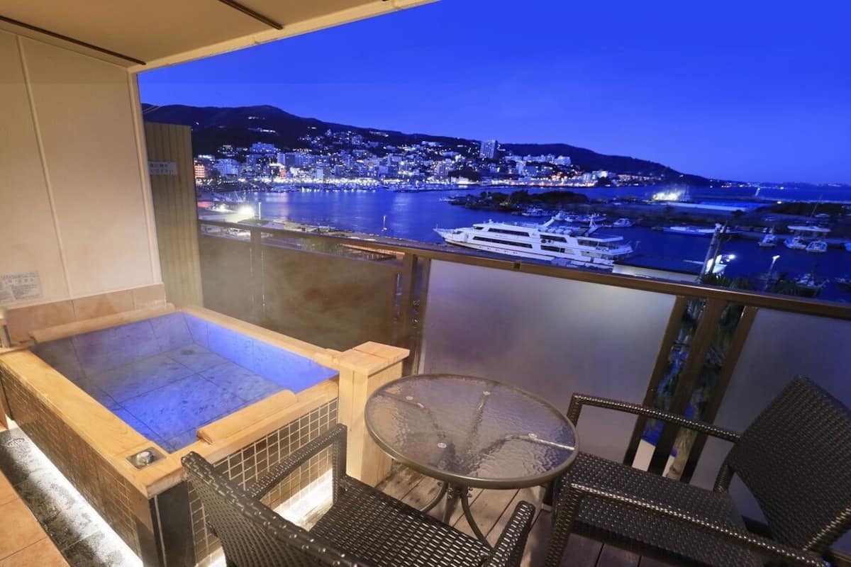 Un balcon avec un jacuzzi, une table et des chaises, donnant sur une vue panoramique de la ville la nuit.