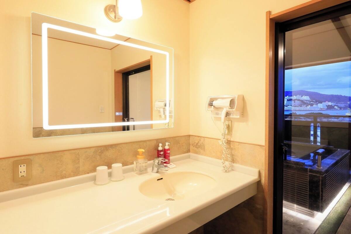 Une salle de bain d’hôtel avec un grand miroir, un lavabo et un sèche-cheveux fixé au mur.