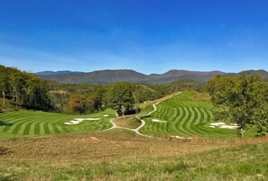 Ein Golfplatz mit gepflegten Fairways und Greens, umgeben von Bäumen und Bergen.