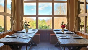 Ruokailutilassa on neljälle henkilölle katetut puupöydät, suuret ikkunat ja näkymä puita ja taivasta vasten.
